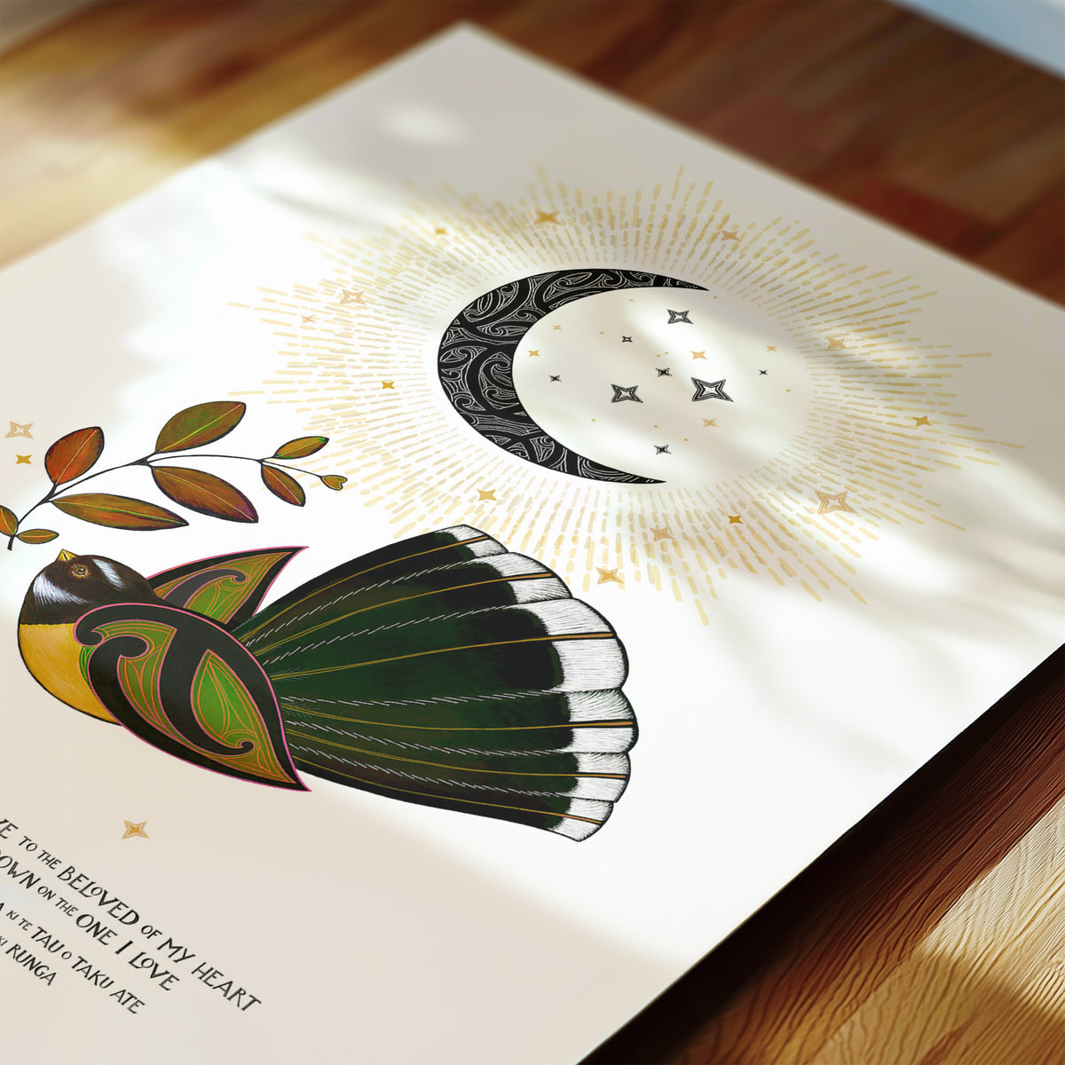 New Zealand pīwakawaka art print, E Rere E Te Manu – The Beloved of My Heart, featuring a fantail carrying a leaf of love beneath a crescent moon, with golden rays and stars. Includes a blessing in te reo Māori and English. Close up detail.