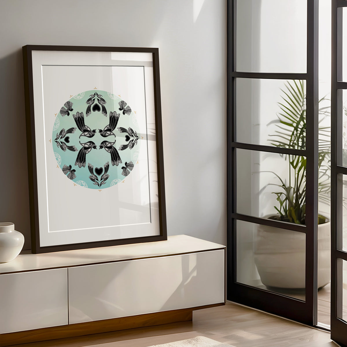 New Zealand bird art print, Manu Mandala by Amber Smith, featuring tūī and pīwakawaka flying together in a circular mandala against a hazy blue background, reflecting the beauty of Aotearoa’s native birds. Living room art from Aotearoa