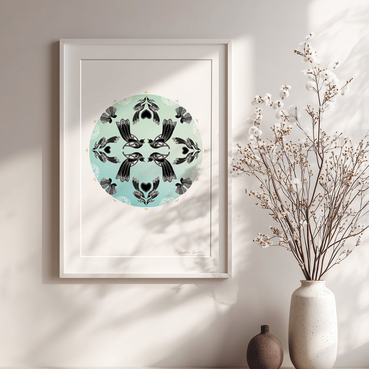 New Zealand bird art print, Manu Mandala by Amber Smith, featuring tūī and pīwakawaka flying together in a circular mandala against a hazy blue background, reflecting the beauty of Aotearoa’s native birds. Framed in white with sunlight and vases of flowers