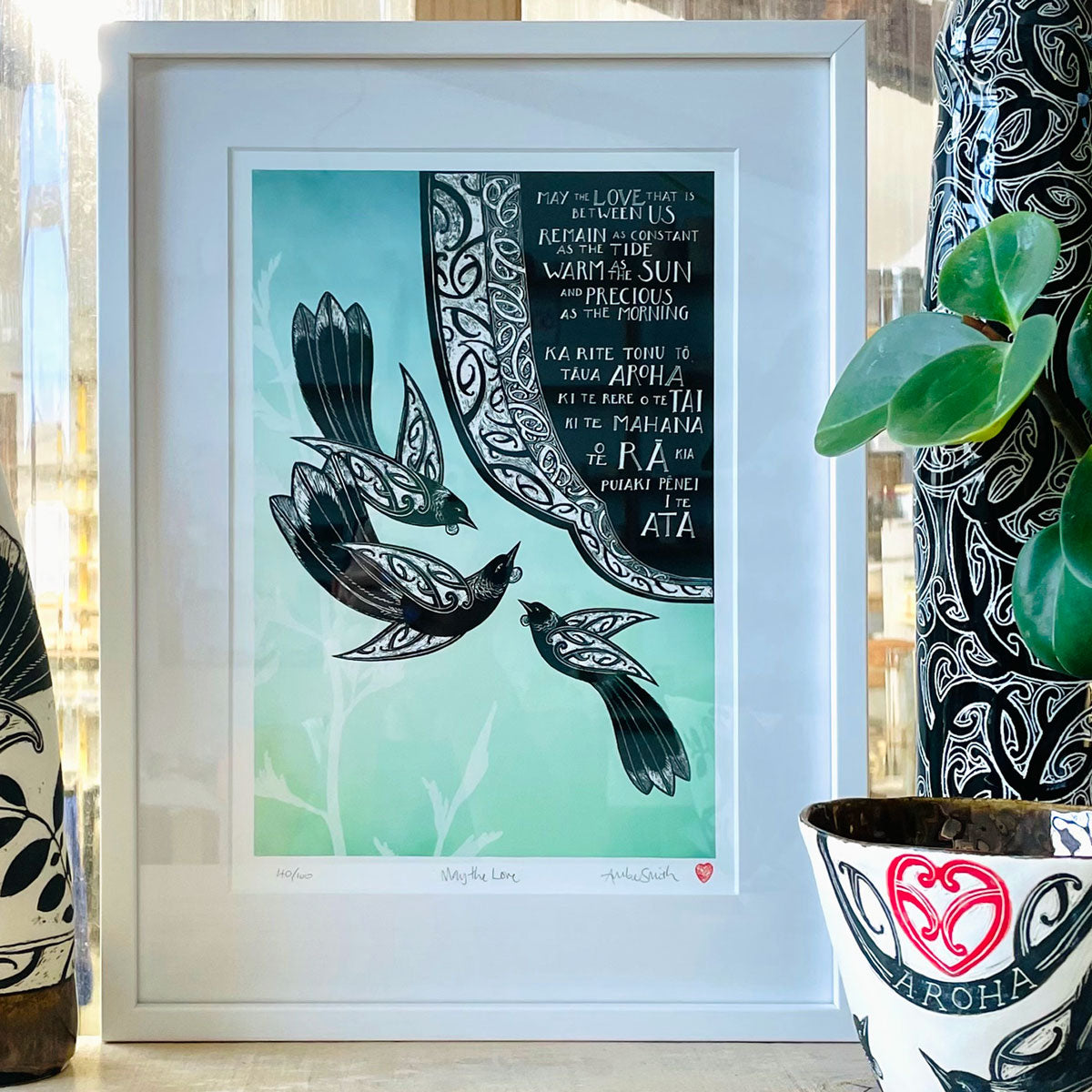 Framed, in studio, May the Love nz art print. Maori art design tui birds and the words May the love that is between us remain as constant as the tide, as warm as the sun, and as precious as the morning in te reo maori and english translation. A blessing karakia print by Amber Smith New Zealand artist