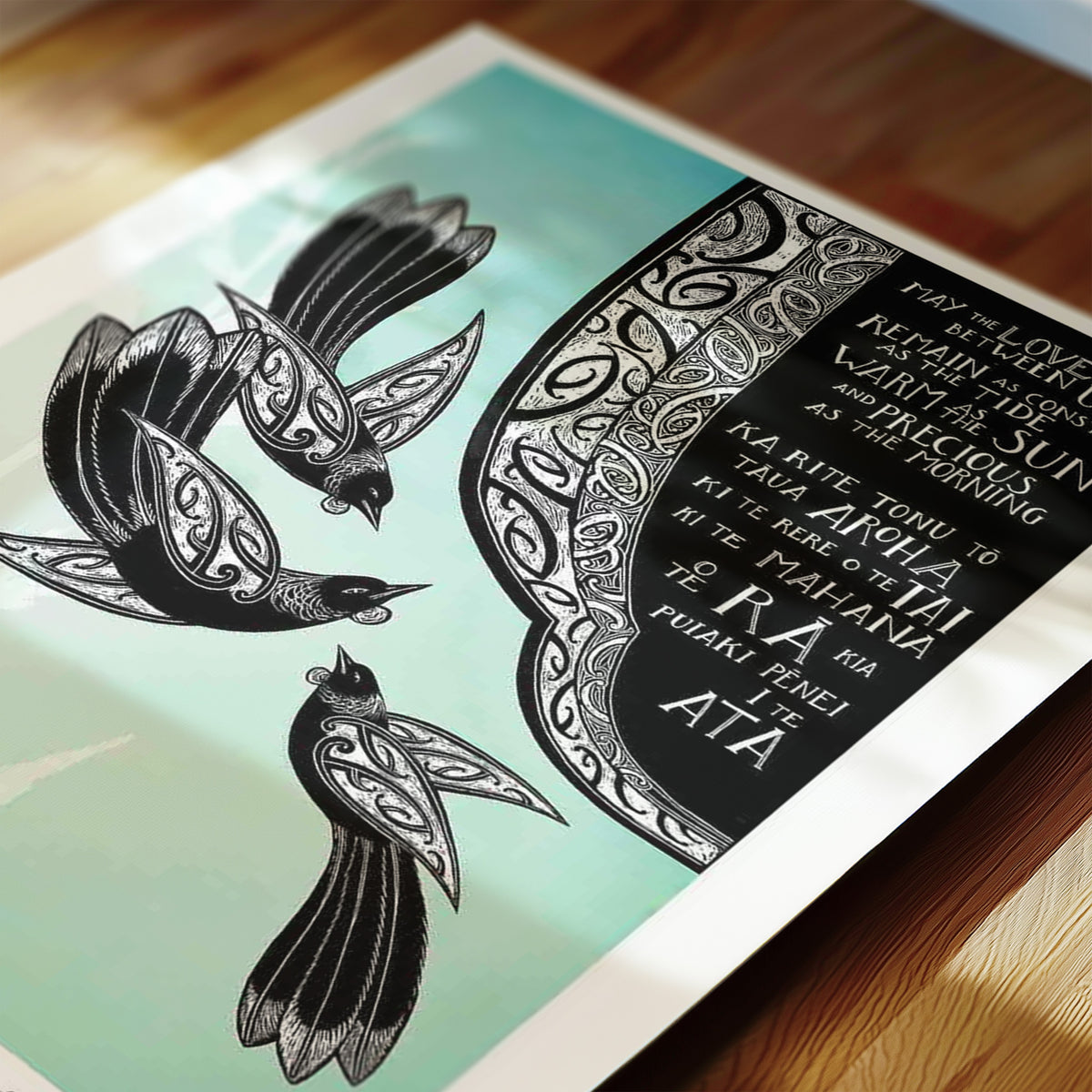 New Zealand tūī art print, May the Love That Is Between Us, featuring three tūī surrounded by kōwhaiwhai patterns, with a bilingual blessing in te reo Māori and English wishing that love remain constant as the tide, warm as the sun and precious as the morning. Close-up detail.