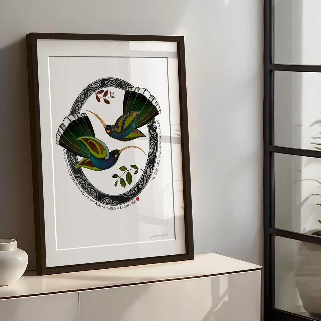 Lounge room framed New Zealand huia bird art print, Tūmanako – Hope, featuring two huia taking flight into the light of a new dawn, with a te reo Māori karakia about the birds calling and the day beginning.