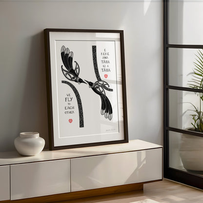 New Zealand tūī art print, We Fly to Each Other, featuring tūī birds and aroha hearts, with a message in te reo Māori and English about finding your way back to each other and being together again. Large size framed and sitting on shelf next to window